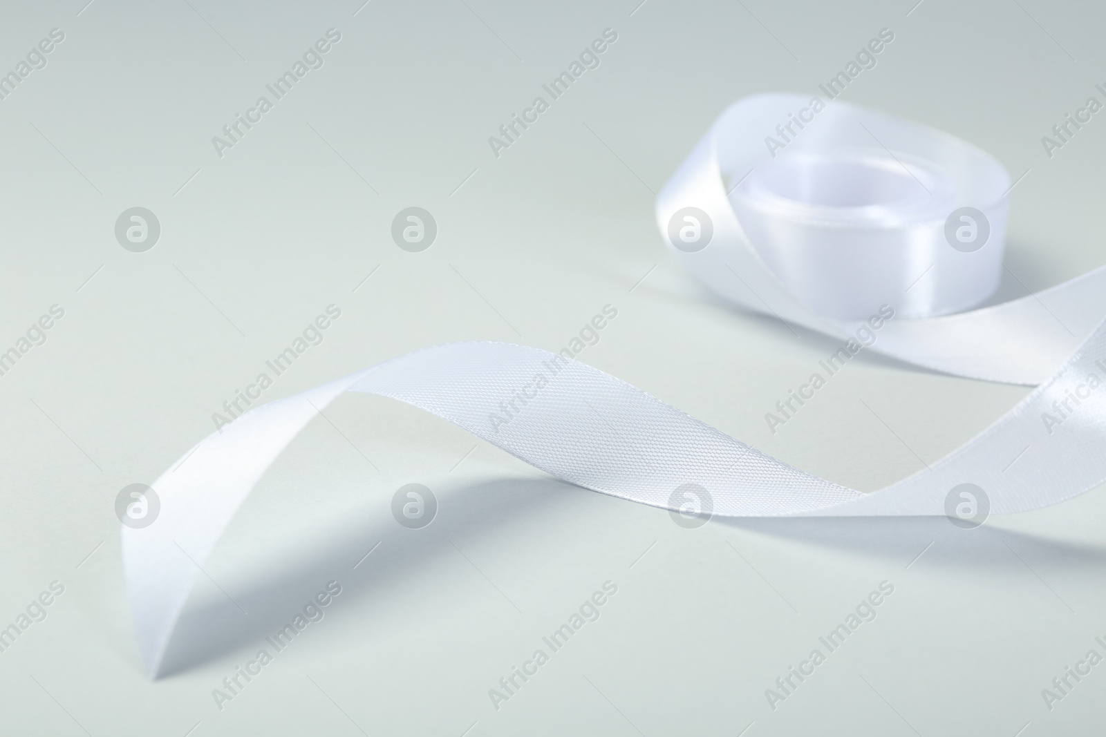 Photo of Beautiful white ribbon reel on light background, closeup