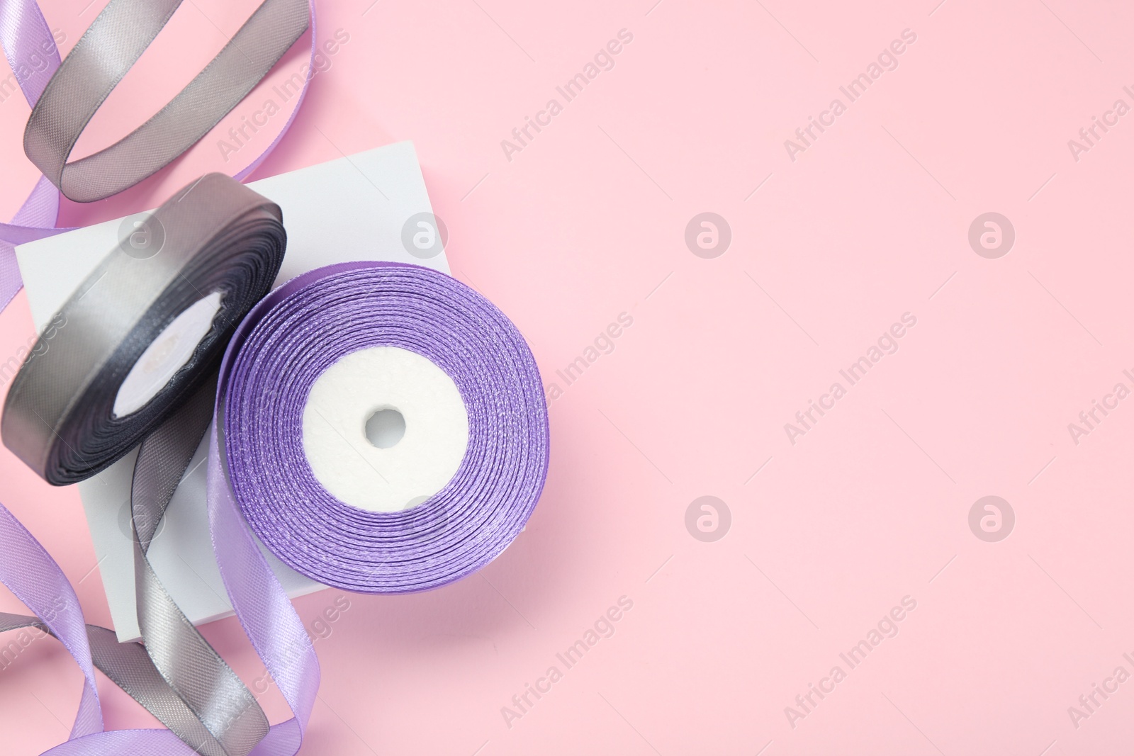 Photo of Ribbon reels in different colors on pink background, top view. Space for text