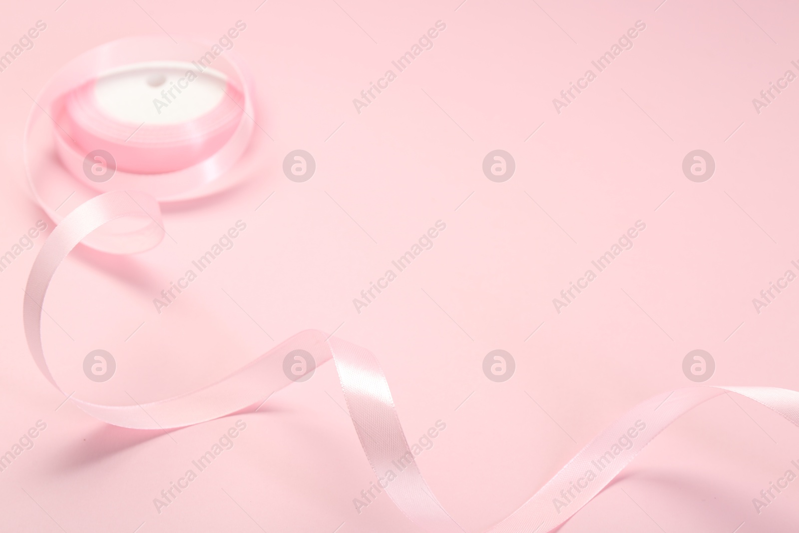 Photo of Beautiful ribbon reel on pink background, closeup. Space for text