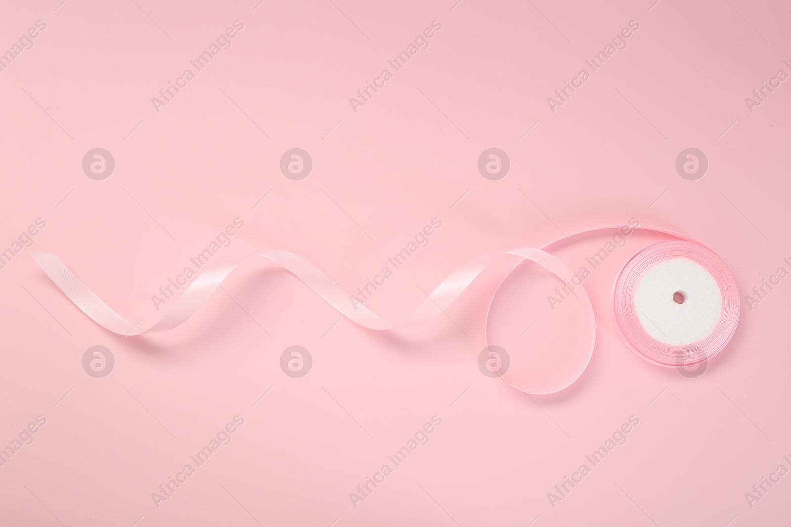 Photo of Beautiful ribbon reel on pink background, top view