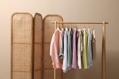 Folding screen and clothing rack with clothes near beige wall indoors