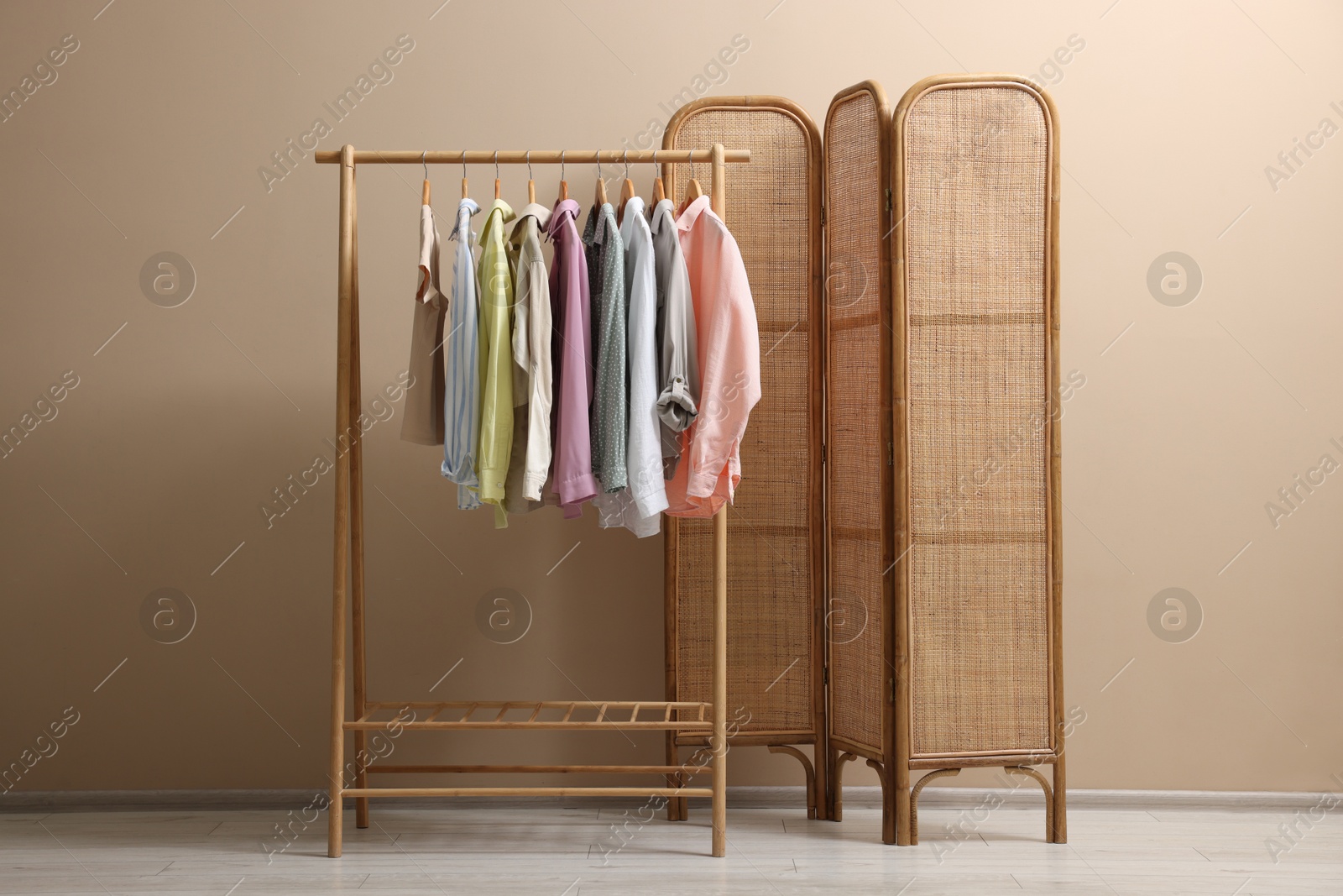 Photo of Folding screen and clothing rack with clothes near beige wall indoors