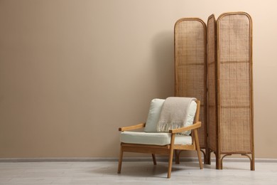 Folding screen, armchair and blanket near beige wall indoors, space for text