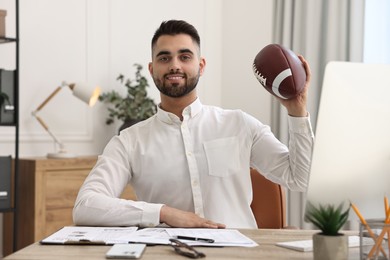 Photo of Young man with american football ball at table in office