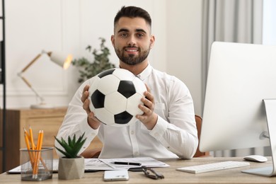 Photo of Young man with soccer ball at table in office