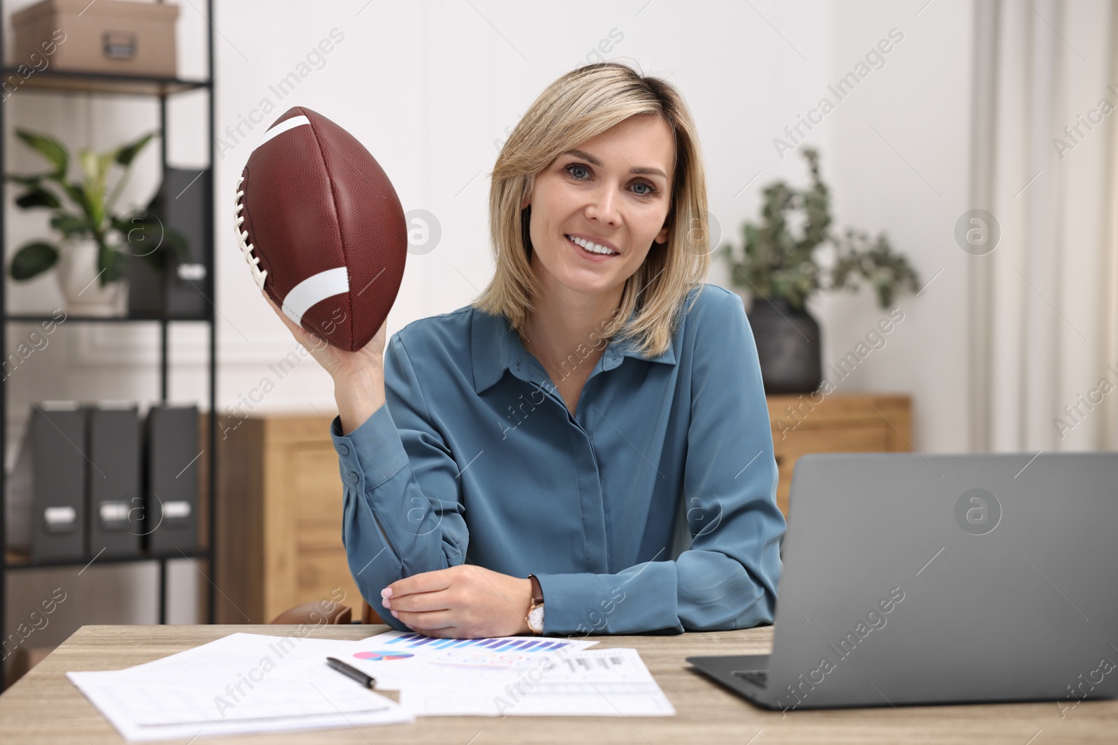 Photo of Smiling woman with american football ball at table in office