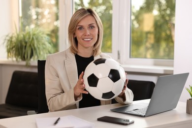 Smiling woman with soccer ball at table in office