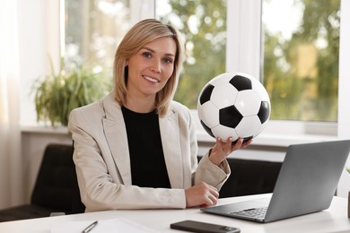 Smiling woman with soccer ball at table in office