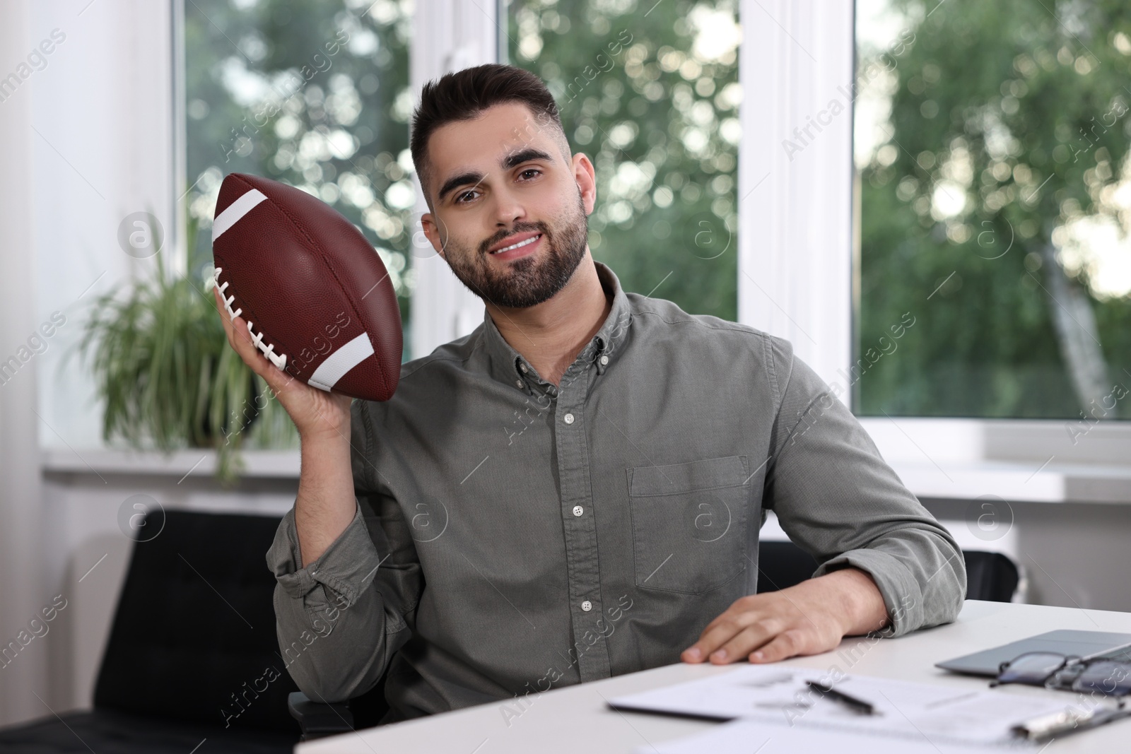 Photo of Young man with american football ball at table in office