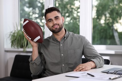 Young man with american football ball at table in office