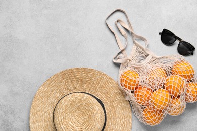 Photo of String bag with oranges, sunglasses and straw hat on grey table, top view. Space for text