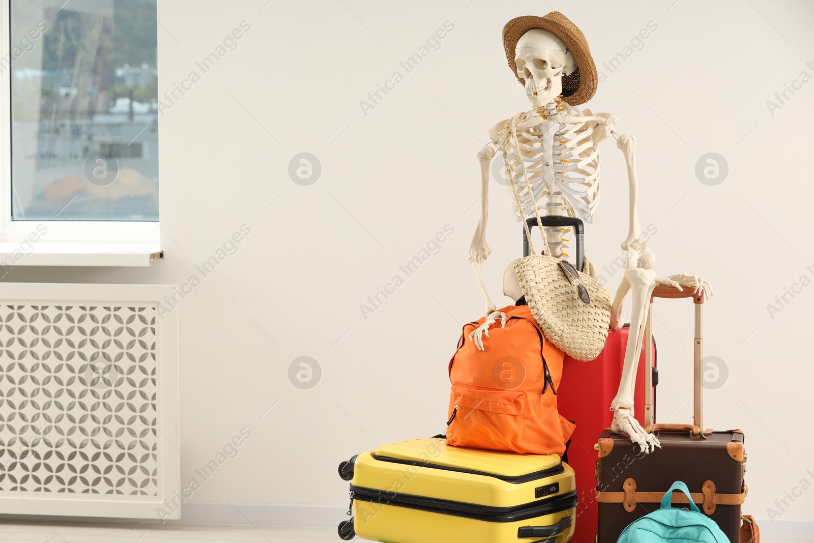 Photo of Waiting concept. Human skeleton in hat with suitcases indoors