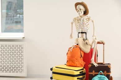 Waiting concept. Human skeleton in hat with suitcases indoors