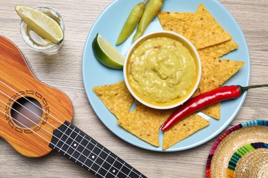 Guacamole, nachos chips, tequila, Mexican sombrero hat and ukulele on wooden table, flat lay