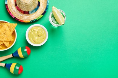 Photo of Mexican sombrero hat, guacamole, nachos chips, maracas and tequila on green background, flat lay. Space for text