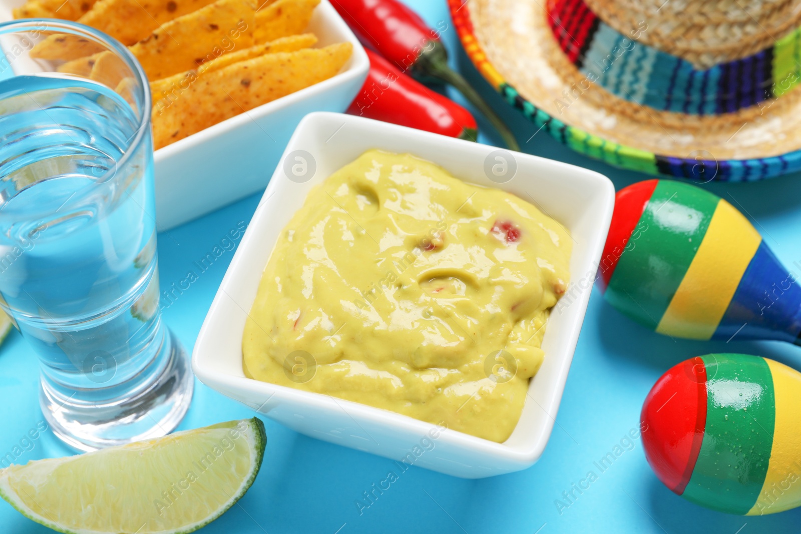 Photo of Guacamole, tequila, lime, maracas, nachos chips and Mexican sombrero hat on light blue background, closeup