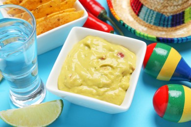 Guacamole, tequila, lime, maracas, nachos chips and Mexican sombrero hat on light blue background, closeup
