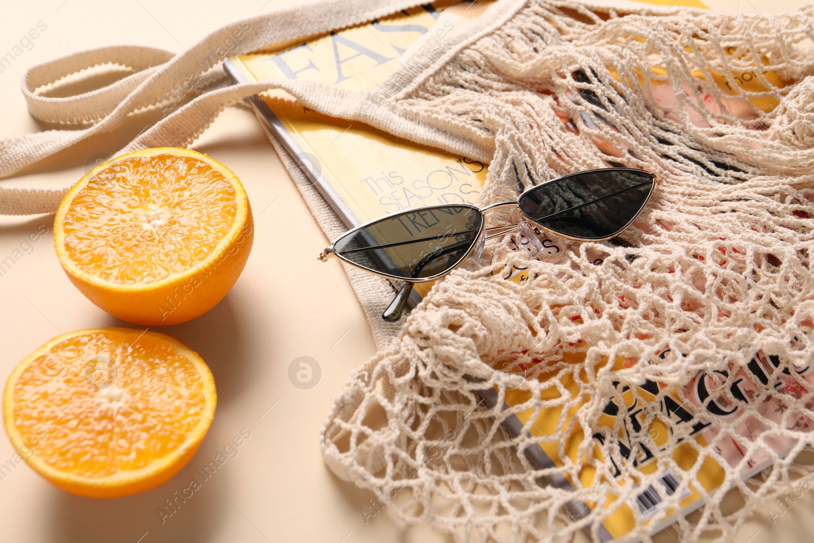 Photo of String bag, magazine, sunglasses and halves of orange on beige background