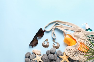 String bag and different beach accessories on light blue background, flat lay. Space for text