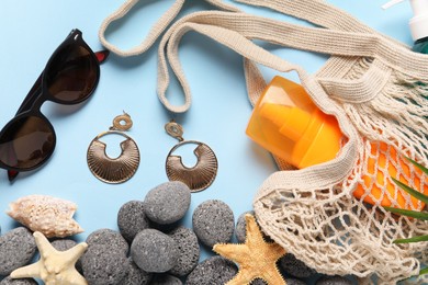 Photo of String bag and different beach accessories on light blue background, flat lay