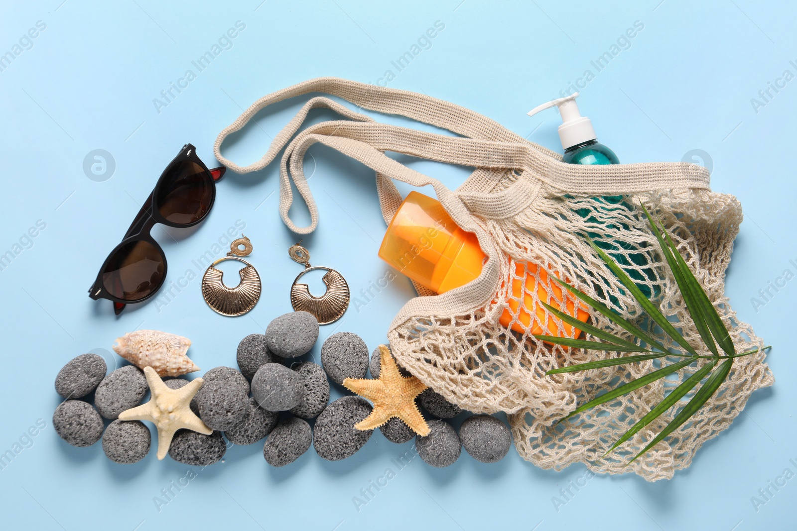 Photo of String bag and different beach accessories on light blue background, flat lay