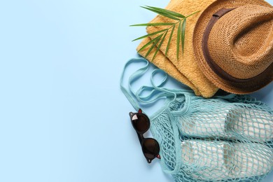 String bag, different beach accessories and palm leaf on light blue background, flat lay. Space for text