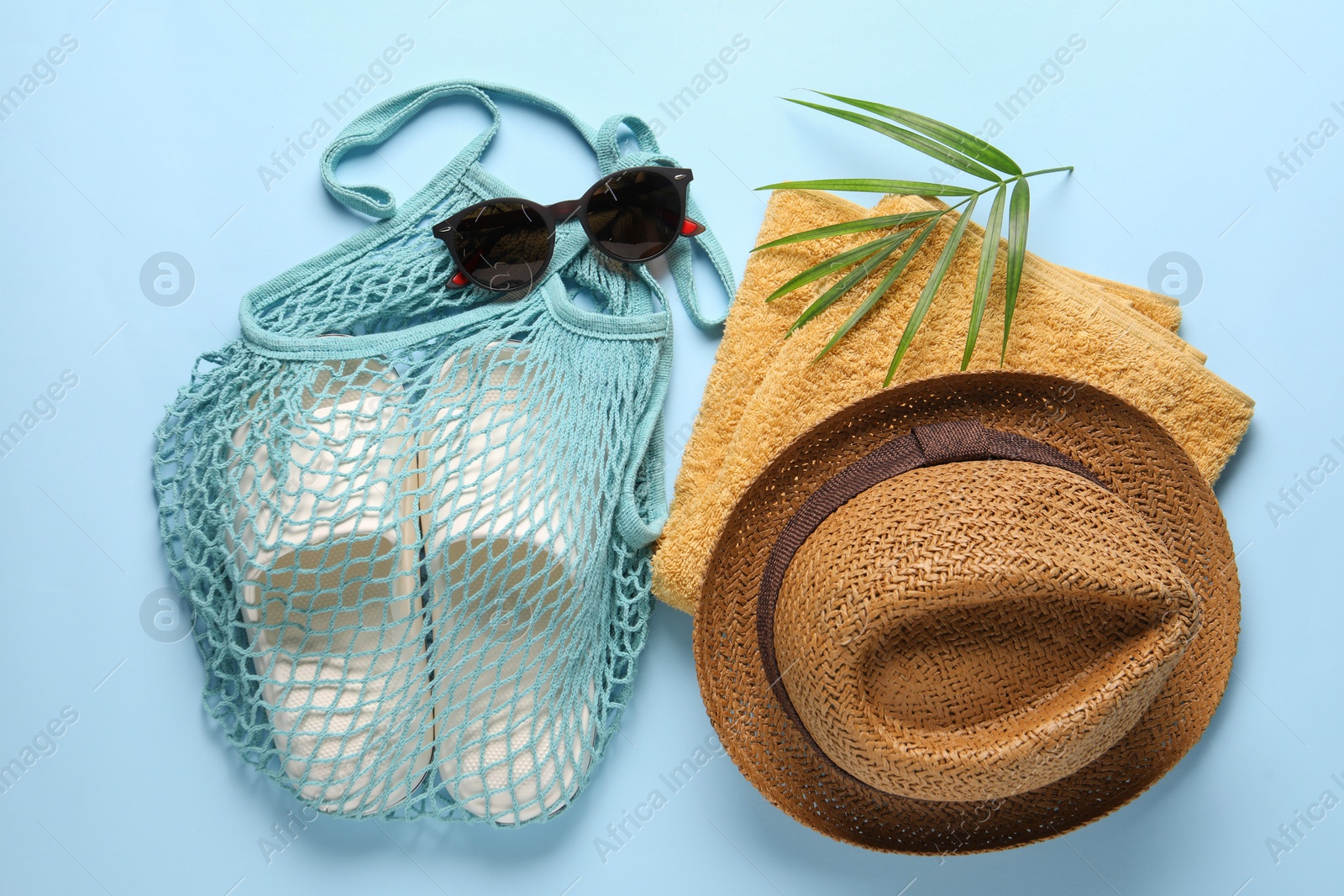 Photo of String bag, different beach accessories and palm leaf on light blue background, flat lay