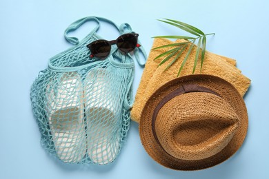 String bag, different beach accessories and palm leaf on light blue background, flat lay