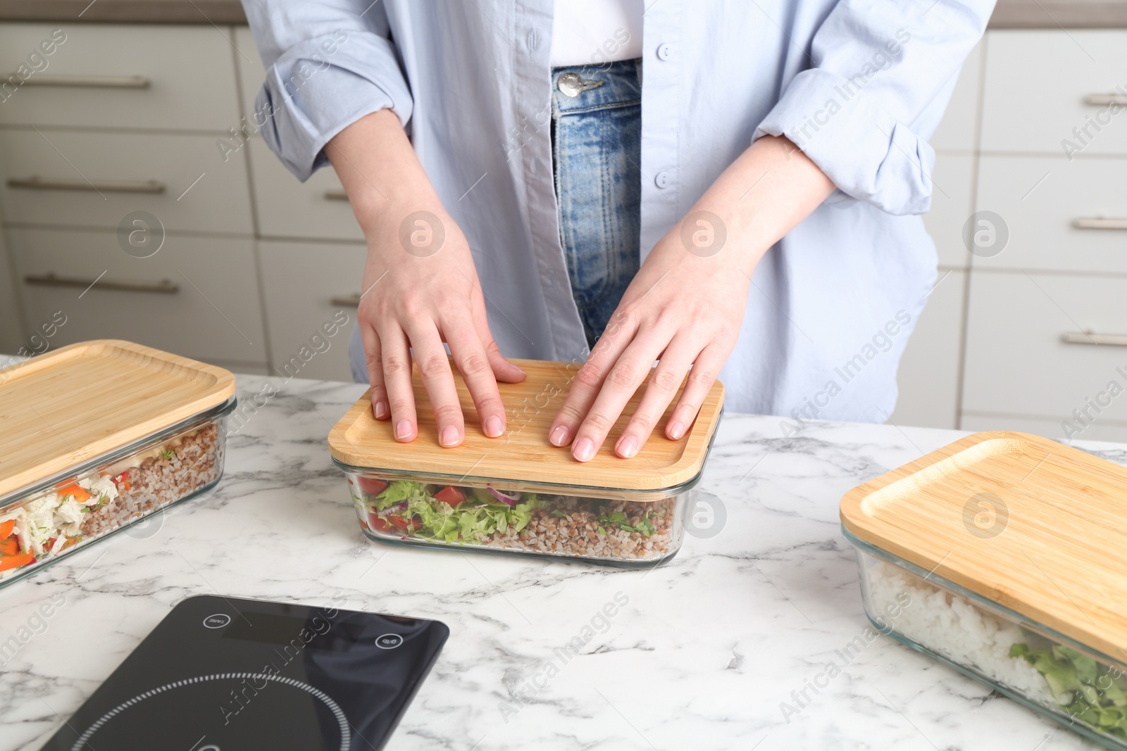 Photo of Healthy food. Woman closing glass container with meal at white marble table, closeup