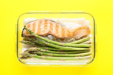 Photo of Healthy meal. Fresh asparagus, salmon and rice in glass container on yellow background, top view