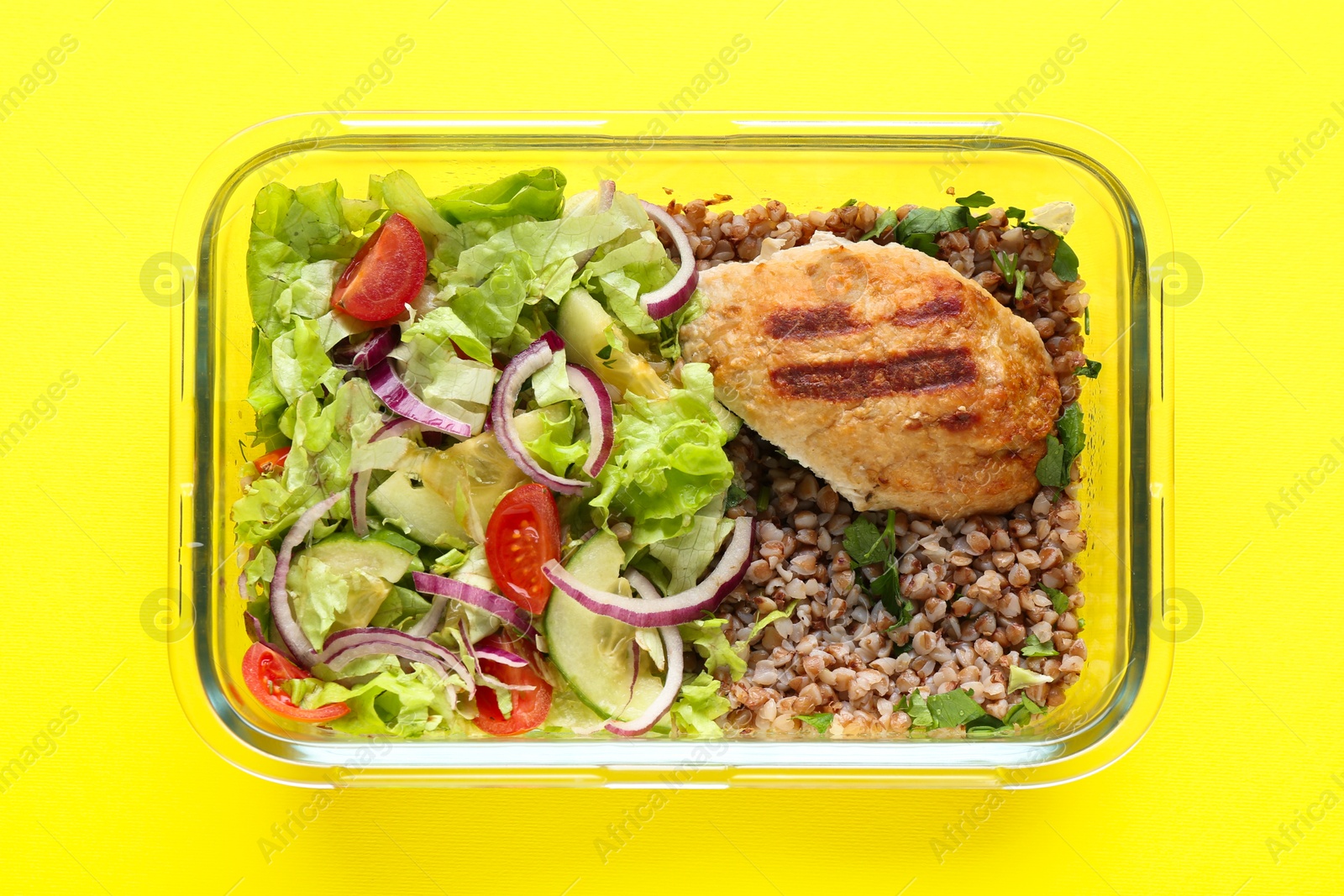 Photo of Healthy meal. Fresh salad, cutlet and buckwheat in glass container on yellow background, top view