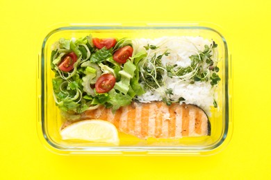 Photo of Healthy meal. Fresh salad, salmon and rice in glass container on yellow background, top view