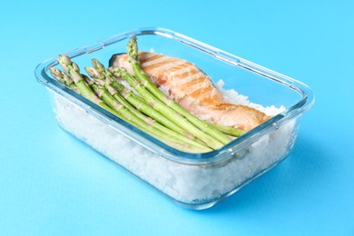 Photo of Healthy meal. Fresh asparagus, salmon and rice in glass container on light blue background