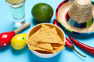 Photo of Mexican sombrero hat, nachos chips, maracas, tequila and chili pepper on light blue background