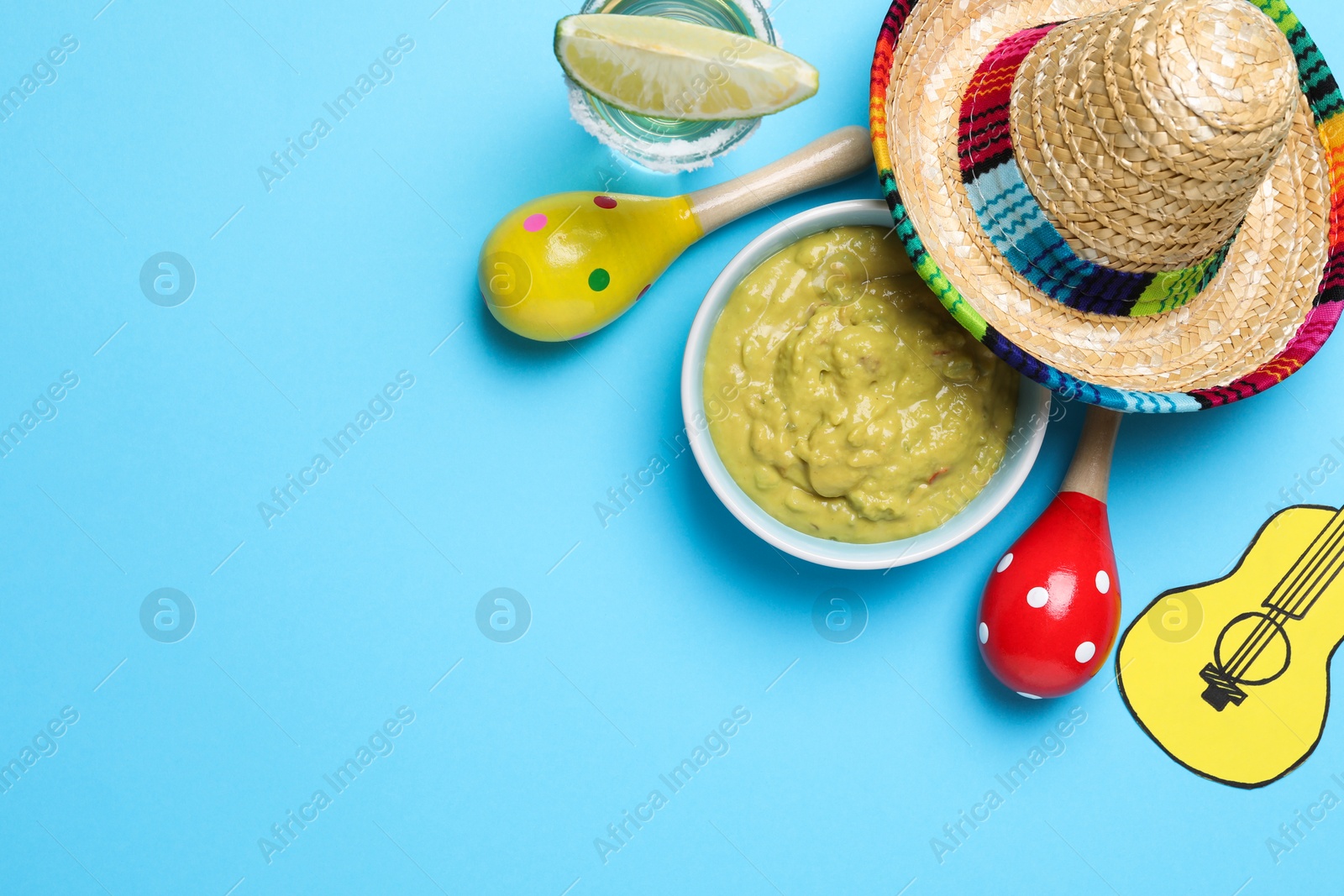 Photo of Mexican sombrero hat, guacamole, maracas, tequila and paper guitar on light blue background, flat lay. Space for text