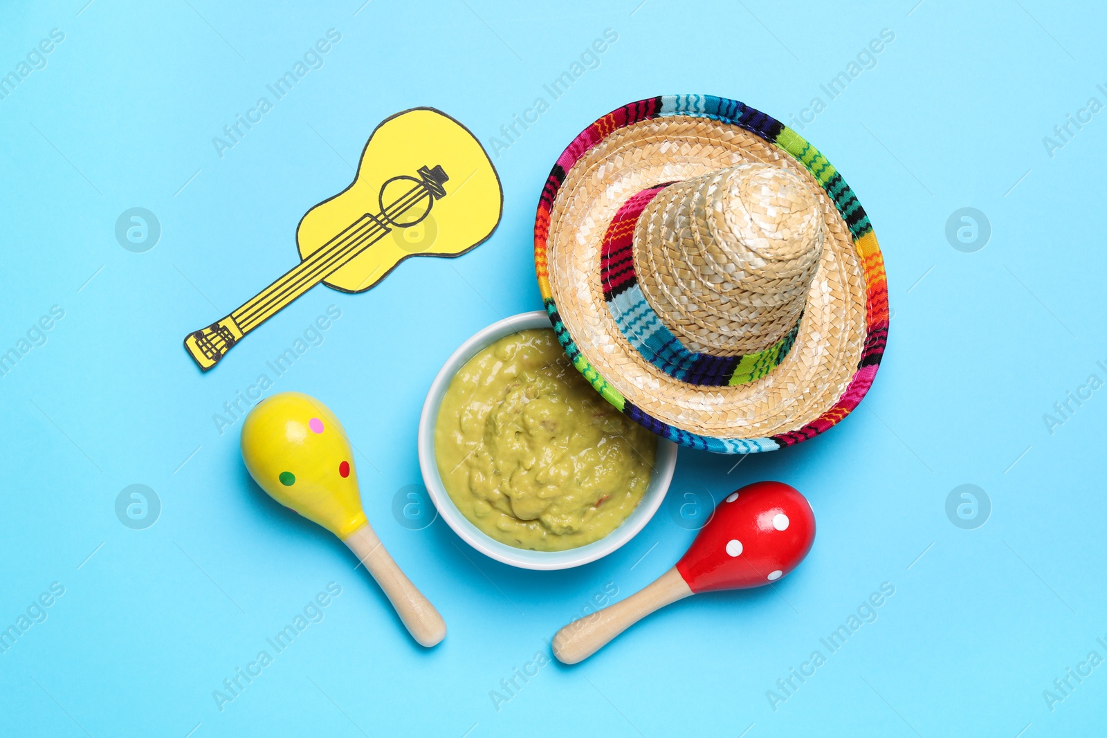 Photo of Mexican sombrero hat, guacamole, maracas and paper guitar on light blue background, flat lay
