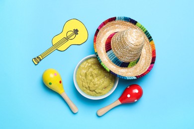 Photo of Mexican sombrero hat, guacamole, maracas and paper guitar on light blue background, flat lay