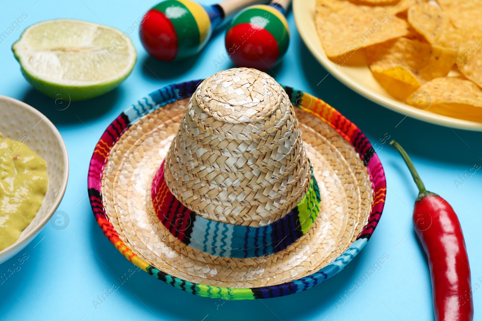 Photo of Mexican sombrero hat, chili pepper, maracas and nachos chips on light blue background