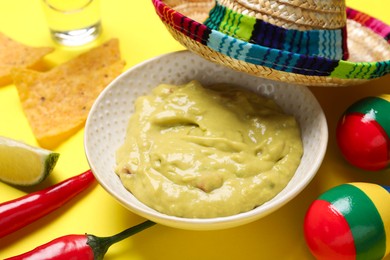 Photo of Guacamole, Mexican sombrero hat, nachos chips, maracas and chili pepper on yellow background, closeup
