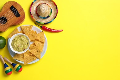 Mexican sombrero hat, nachos chips, guacamole, maracas and ukulele on yellow background, flat lay. Space for text