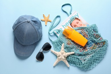 String bag and different beach accessories on light blue background, flat lay