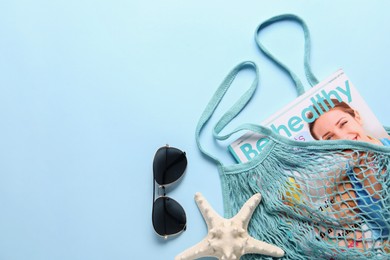 String bag, sunglasses, starfish and magazine on light blue background, top view. Space for text