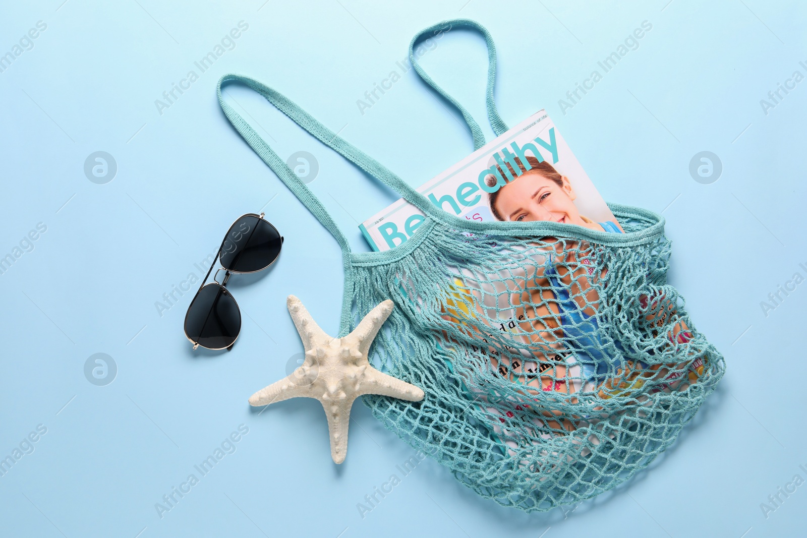 Photo of String bag, sunglasses, starfish and magazine on light blue background, top view