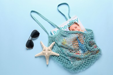 Photo of String bag, sunglasses, starfish and magazine on light blue background, top view