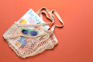 Photo of String bag, sunglasses and magazine on coral background, top view. Space for text