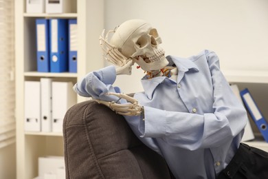 Waiting concept. Human skeleton sitting in armchair at office