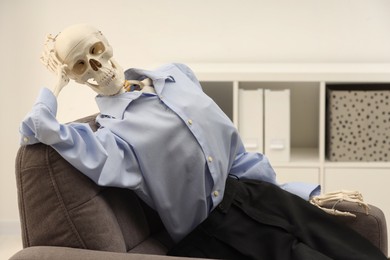 Waiting concept. Human skeleton sitting in armchair at office