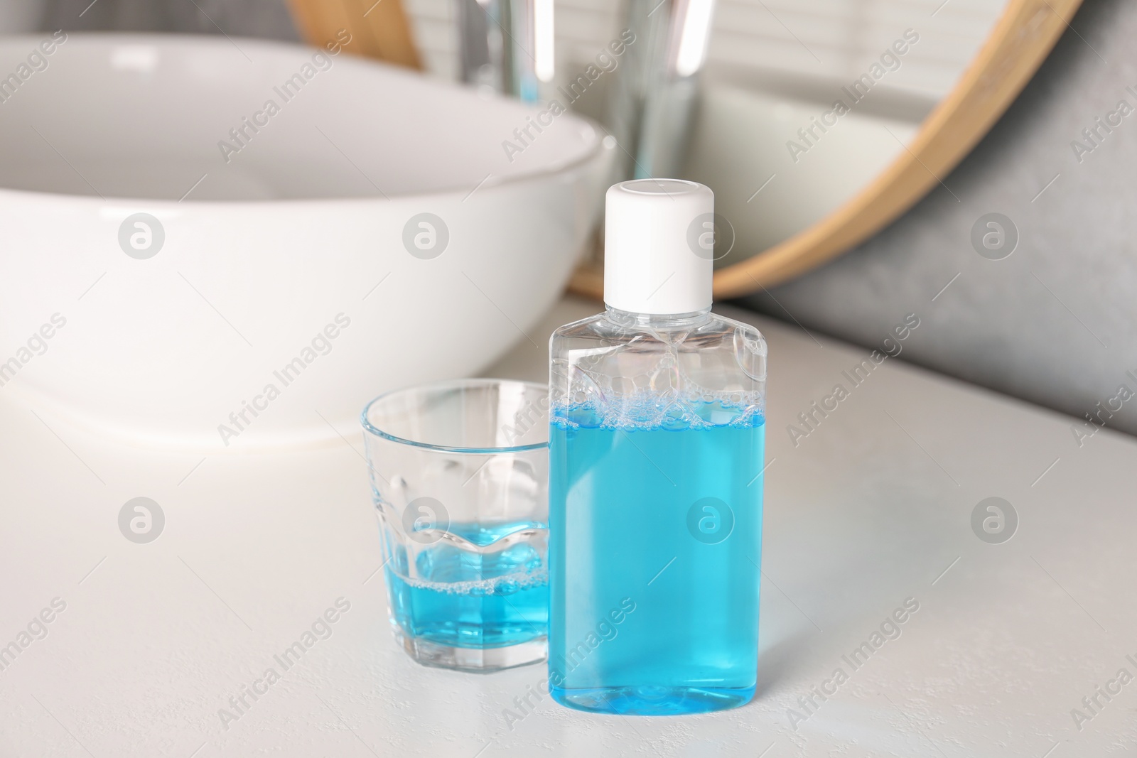 Photo of Bottle and glass of mouthwash on white countertop in bathroom