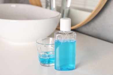 Photo of Bottle and glass of mouthwash on white countertop in bathroom