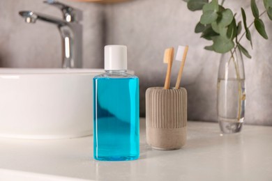 Bottle of mouthwash and toothbrushes on white countertop in bathroom